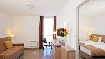 A hotel room with a bed, a desk, a chair, a sofa, and a TV.