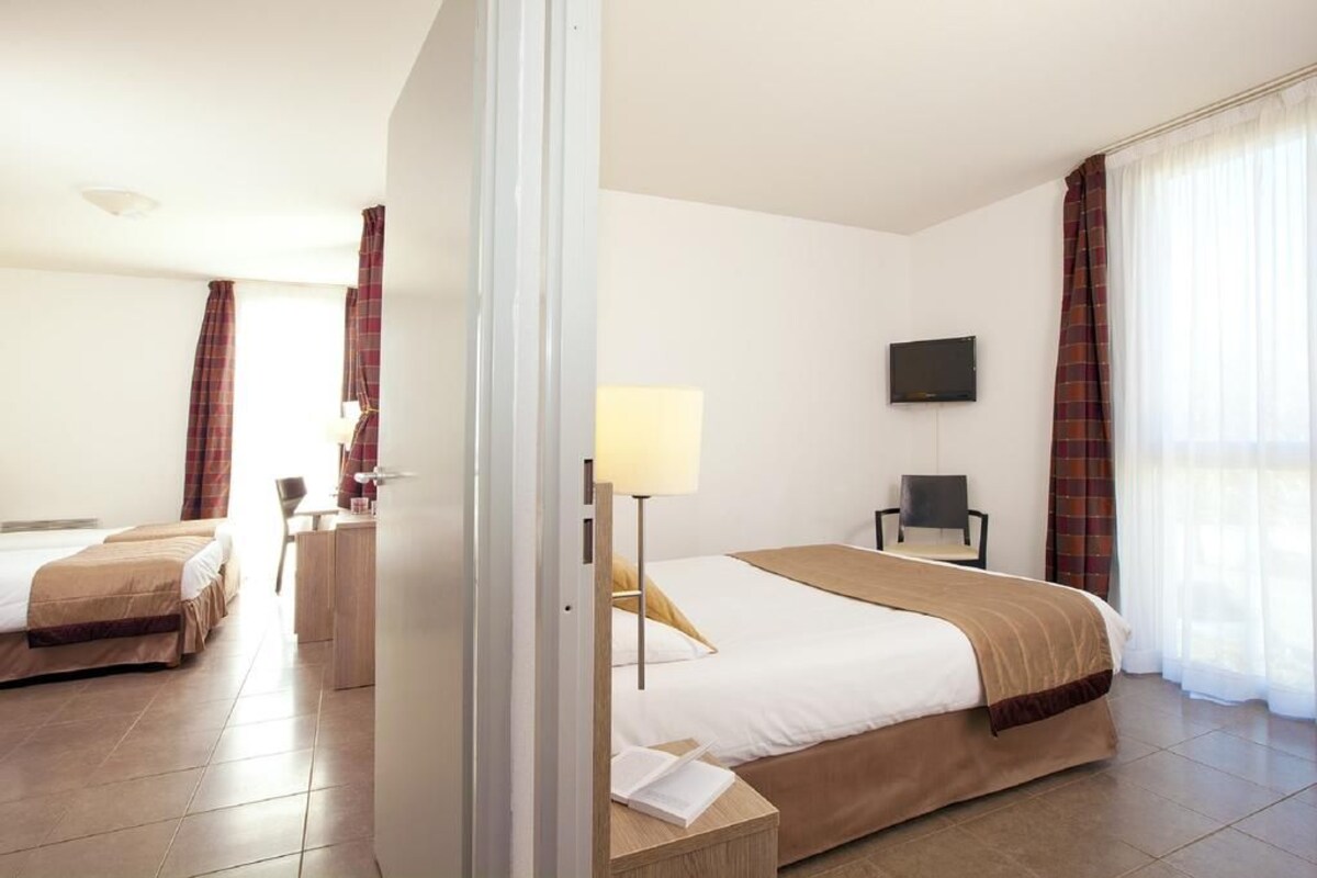 Ein Hotelzimmer mit zwei Betten, einem Schreibtisch, einem Stuhl, einem Fernseher und einem Fenster mit Vorhängen.