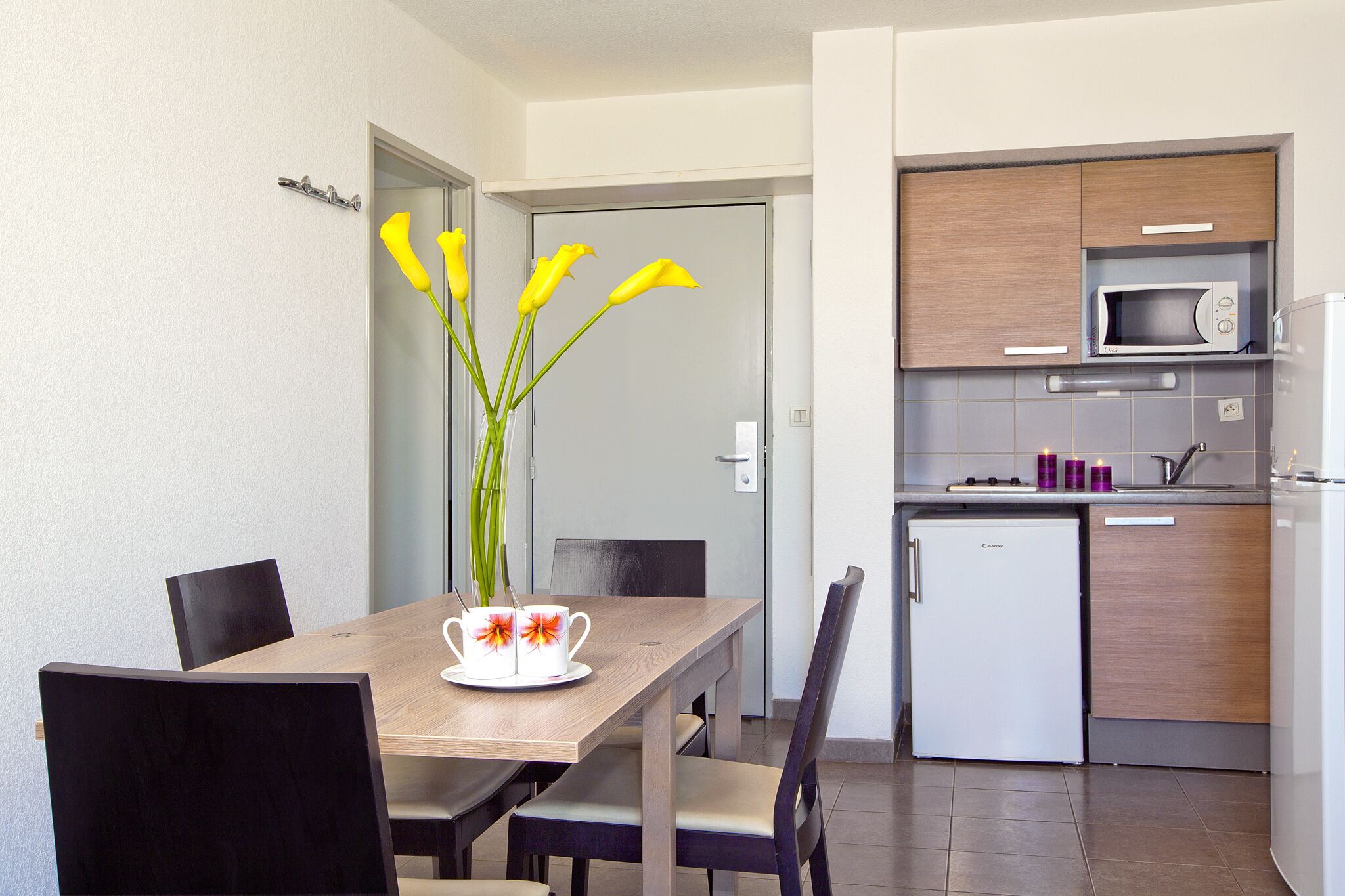 Eine moderne Küche mit Mikrowelle, Kühlschrank und einer kleinen Spüle. Ein Esstisch mit Stühlen und eine Vase mit Blumen sind ebenfalls vorhanden.