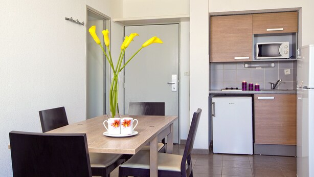Una cocina moderna con microondas, refrigerador y un lavamanos pequeño. Hay una mesa de comedor con sillas y un florero con flores.