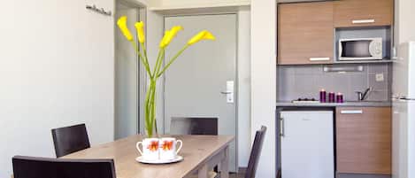 Una cocina moderna con microondas, refrigerador y un lavamanos pequeño. Hay una mesa de comedor con sillas y un florero con flores.