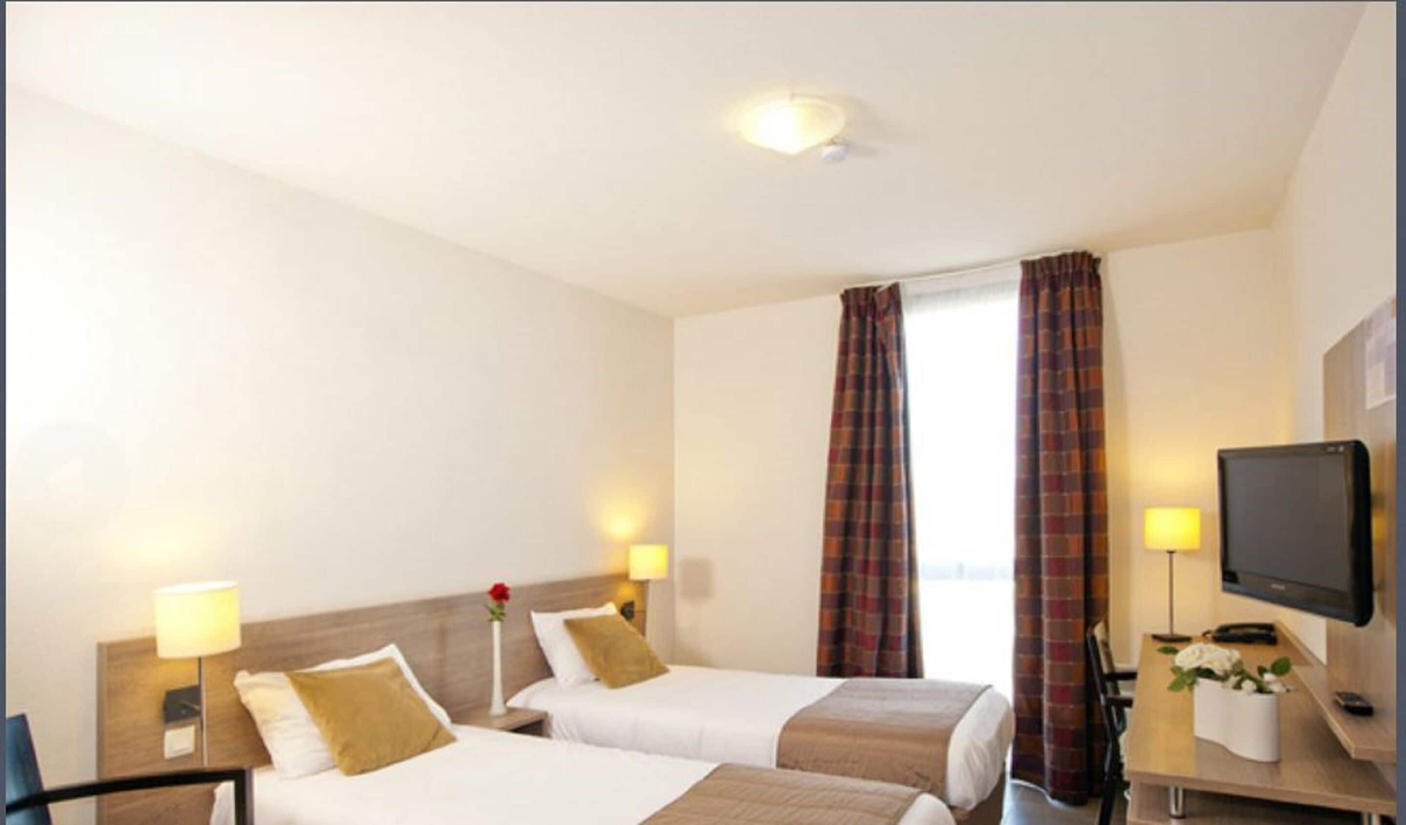 A hotel room with two beds, a television, a desk with a lamp, and a window with curtains.