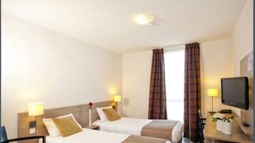 A hotel room with two beds, a television, a desk with a lamp, and a window with curtains.