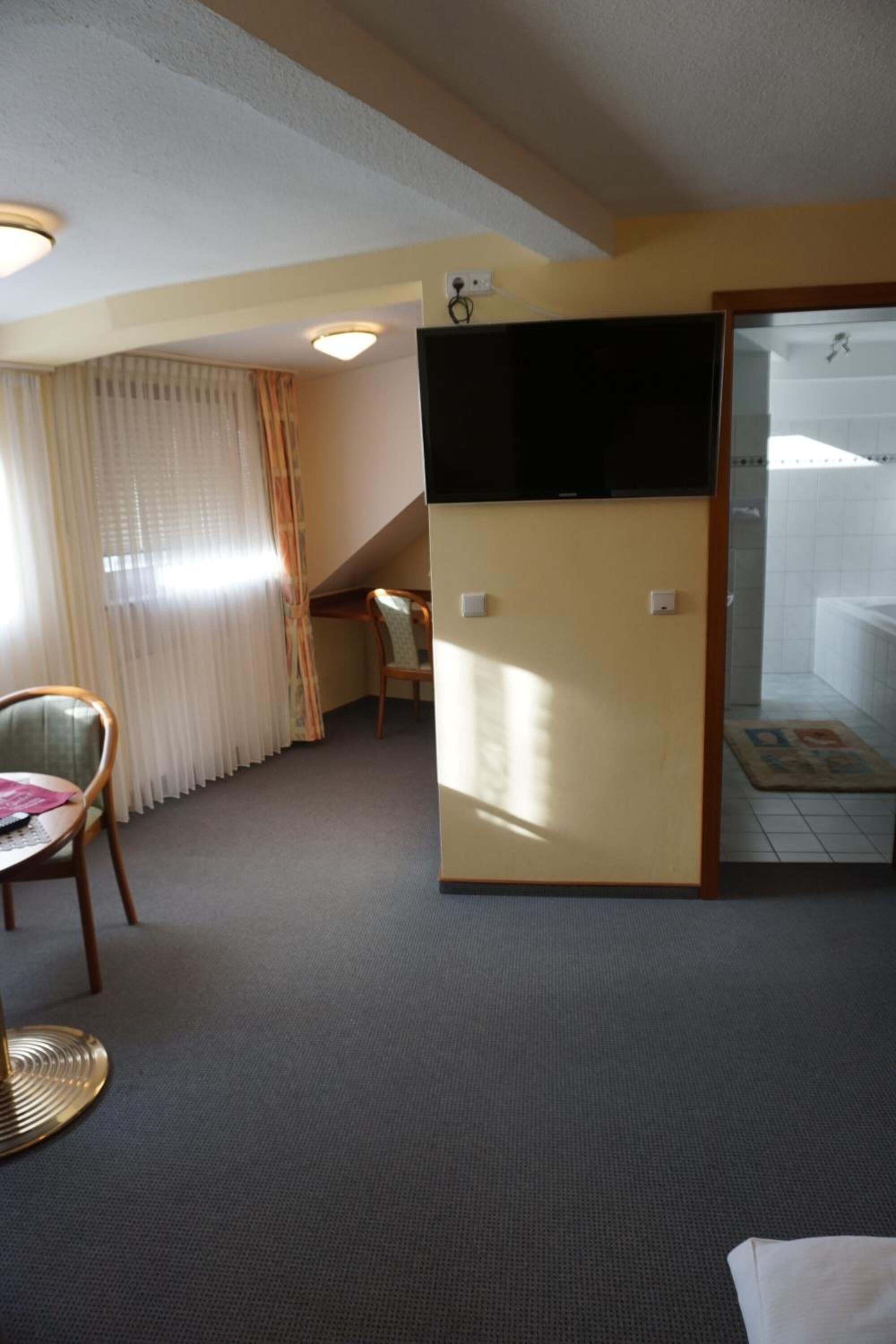 Ein Hotelzimmer mit Bett, Schreibtisch, Stuhl, Fernseher und einem durch eine Glastür sichtbaren Badezimmer.