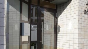 Un ingresso di un edificio con una porta in vetro, una scalinata che vi conduce e un muro rivestito di piastrelle.
