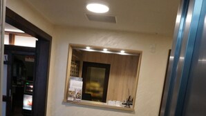 Un'area reception con pavimento in legno, una piccola finestra con un quadro incorniciato e un bancone con il menu.