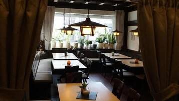 Ein schwach beleuchtetes Restaurant mit hohen Tischen und Stühlen, großen Pendelleuchten und Topfpflanzen.