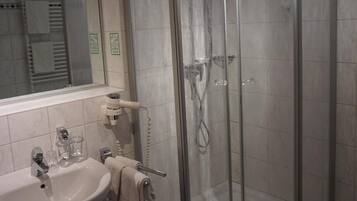 Een badkamer met een douchecabine van glas, een wastafel en een spiegel.