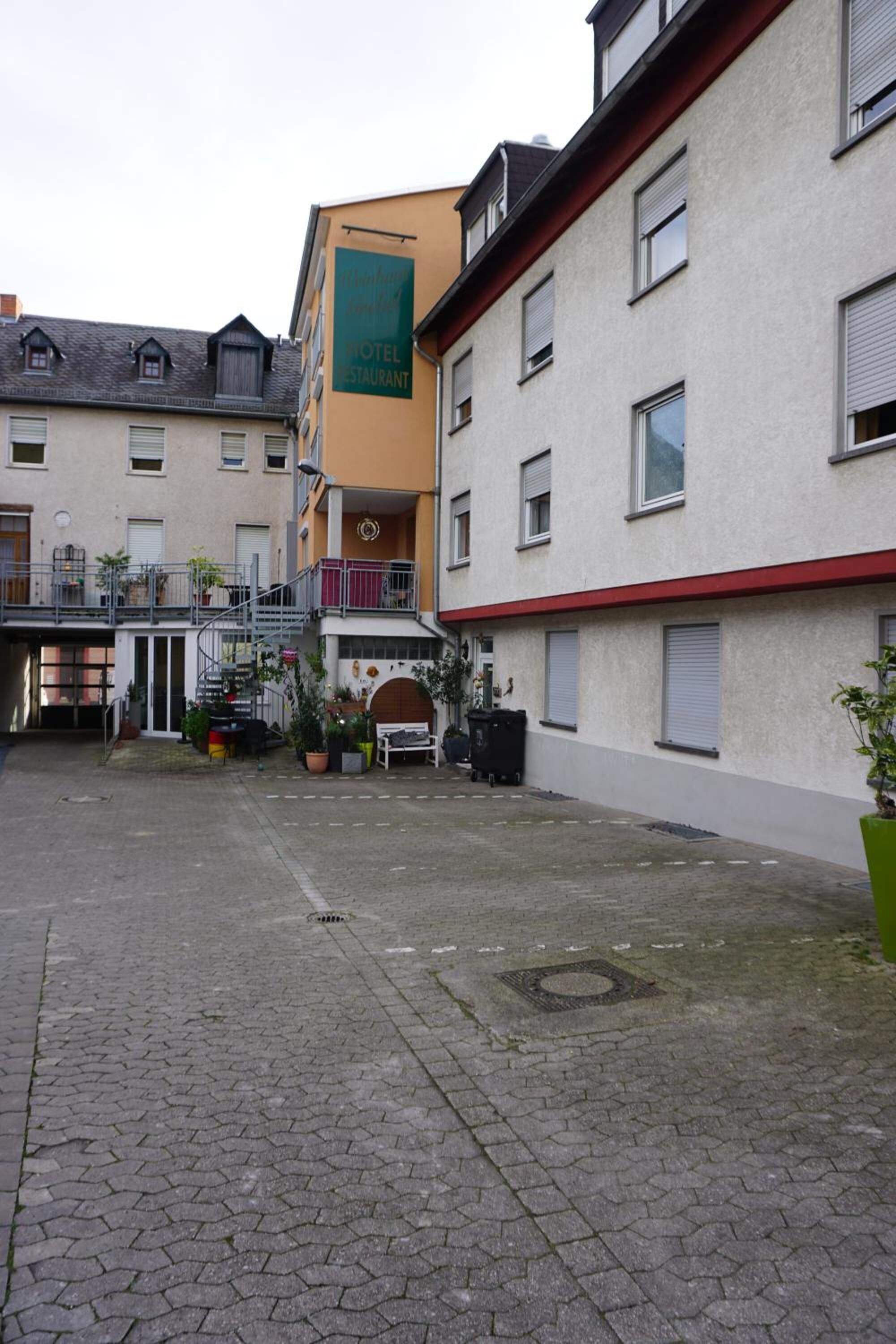 A courtyard with a hotel entrance, potted plants, and a staircase leading to an upper level.