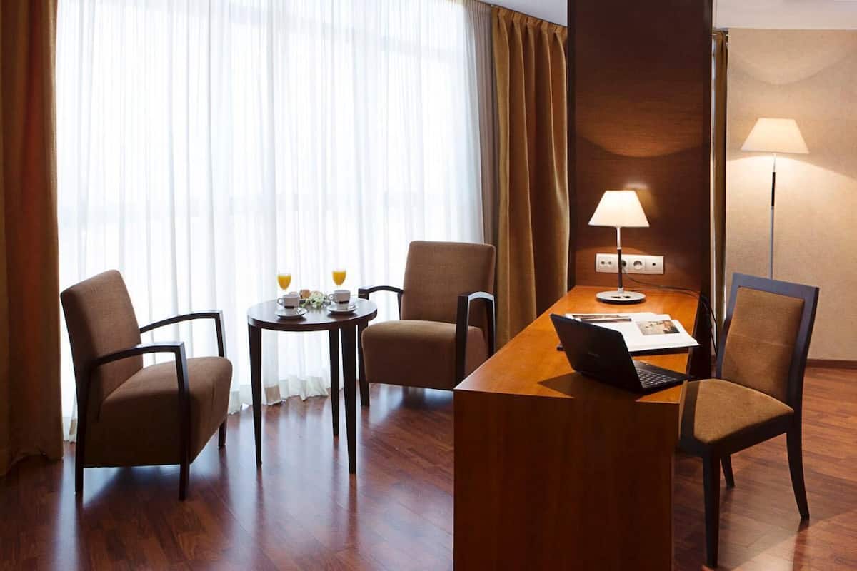 Une chambre d’hôtel comprenant un lit, un bureau avec un ordinateur portable, deux chaises, une table avec une tasse et une soucoupe, et une lampe.