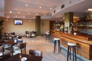 A restaurant with multiple tables and chairs, a bar area with stools, and a television screen mounted on the wall. - Hotel Torre DE Sila (Tordesillas)