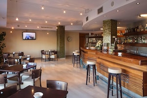 A restaurant with multiple tables and chairs, a bar area with stools, and a television screen mounted on the wall.