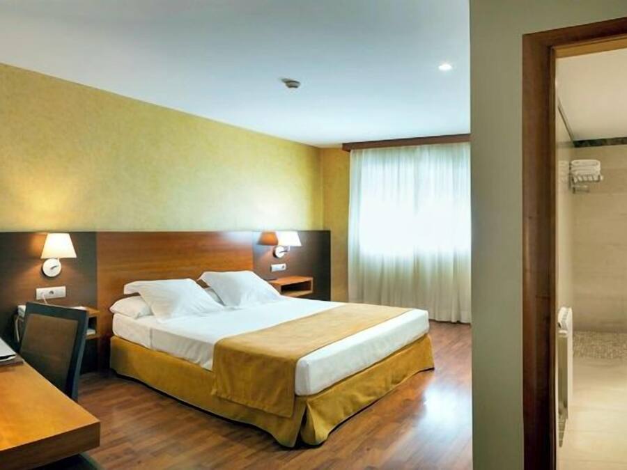 Ein Hotelzimmer mit Bett, Nachttisch, Lampe und Blick ins Badezimmer.