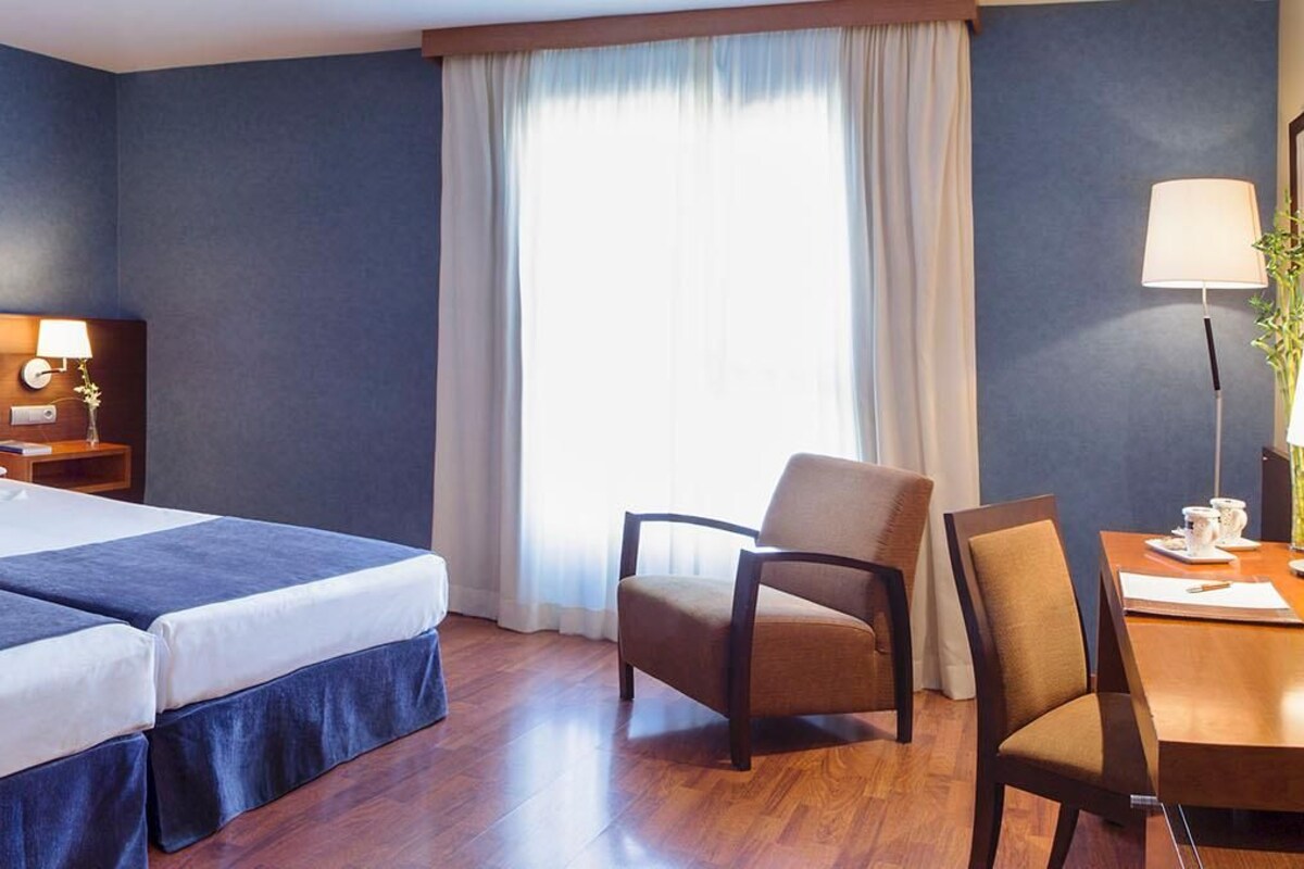 A hotel room with two beds, a desk, a chair, and a TV.