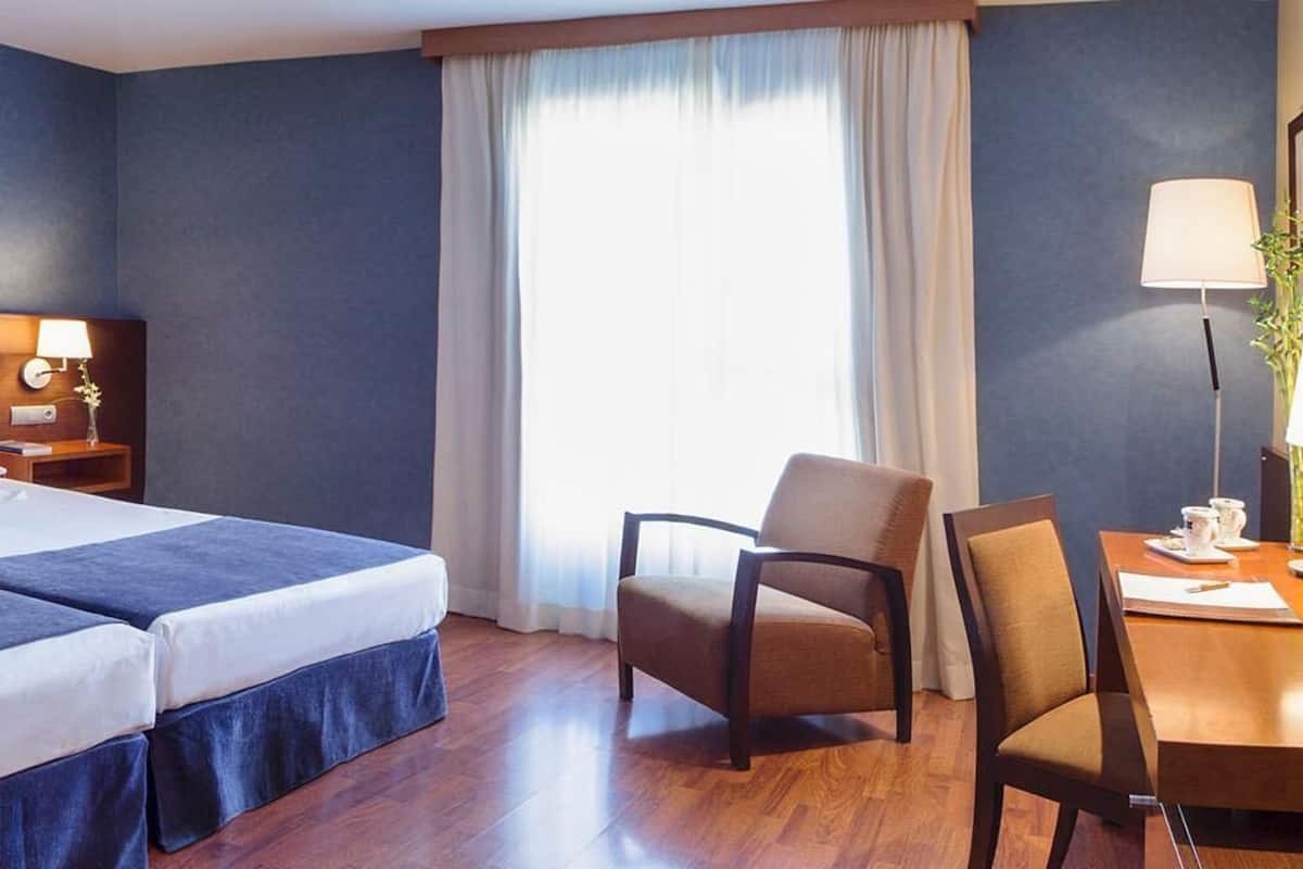 Une chambre d’hôtel avec deux lits, un bureau, une chaise et une télévision.