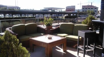 Un espacio al aire libre con mobiliario de mimbre, una mesa y vistas a la ciudad.
