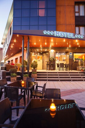 A hotel exterior with a cafe area, outdoor seating, and a staircase leading to the entrance. - Hotel Torre DE Sila (Tordesillas)