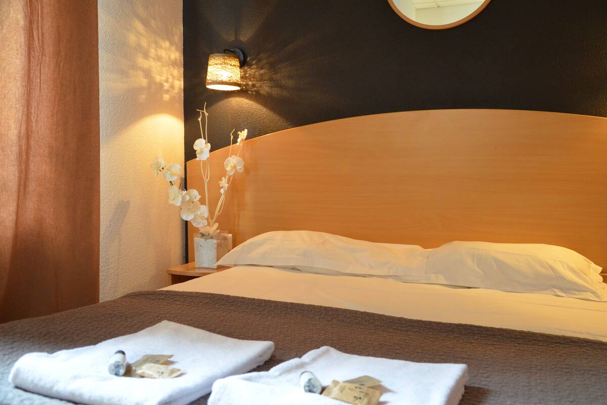 Una cama bien hecha con sábanas blancas, cabecera de madera y lámpara fijada a la pared.