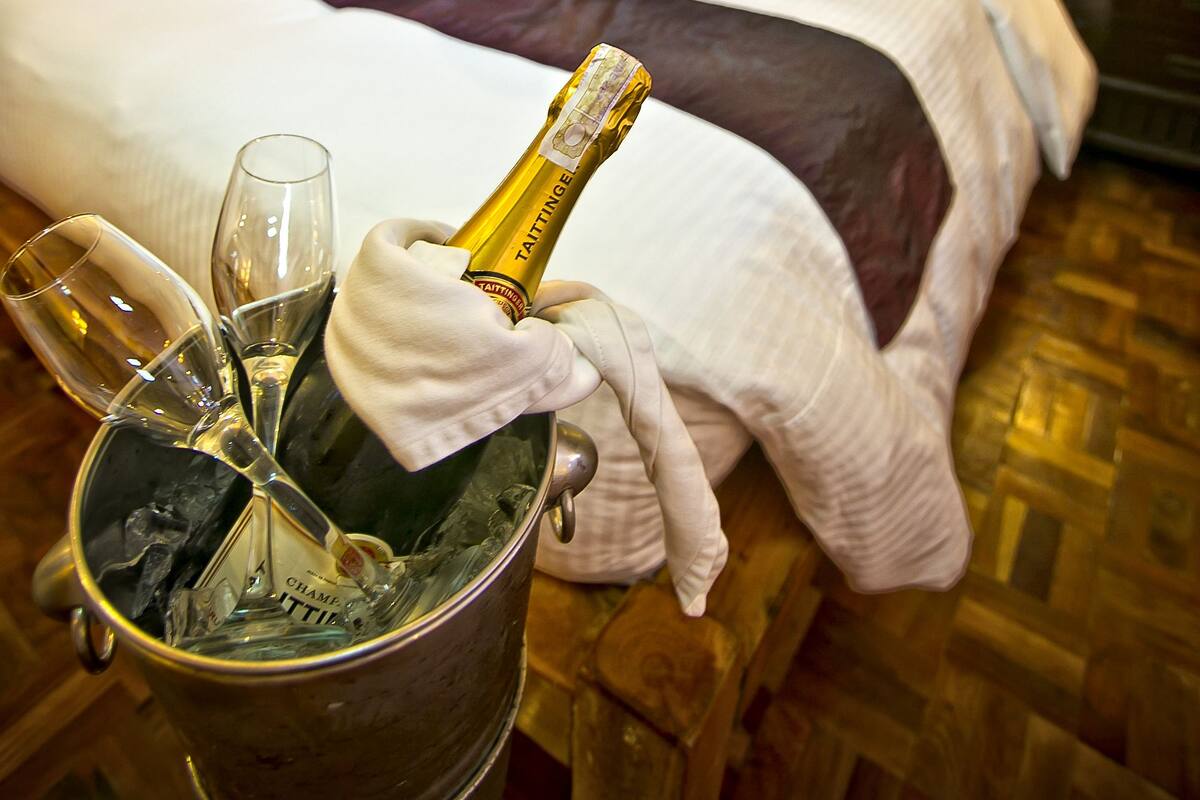 A luxurious hotel room with a bed, a bedside table with a bottle of champagne, and a bucket with glasses.