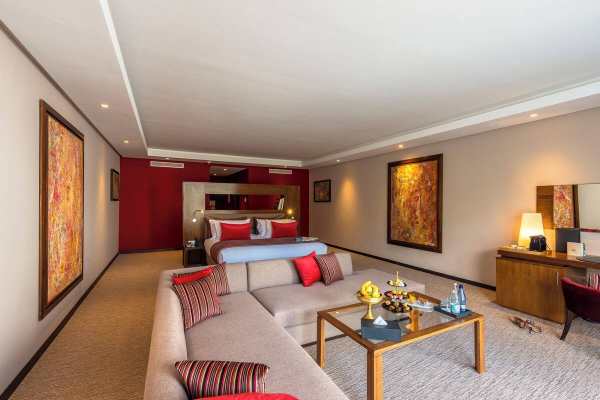 A modern hotel room with a large sofa, a desk, a bed, and artwork on the walls.