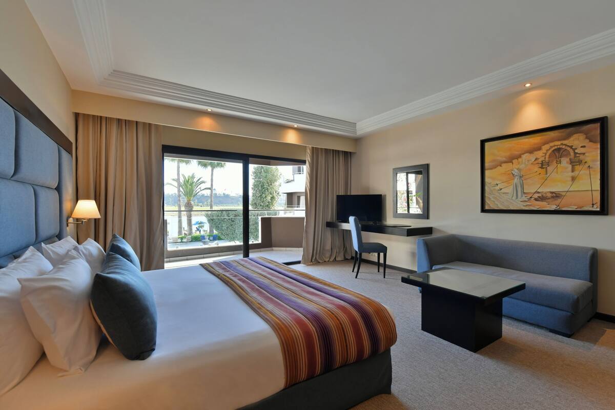 A hotel room with a large bed, a desk, a sofa, and a TV.