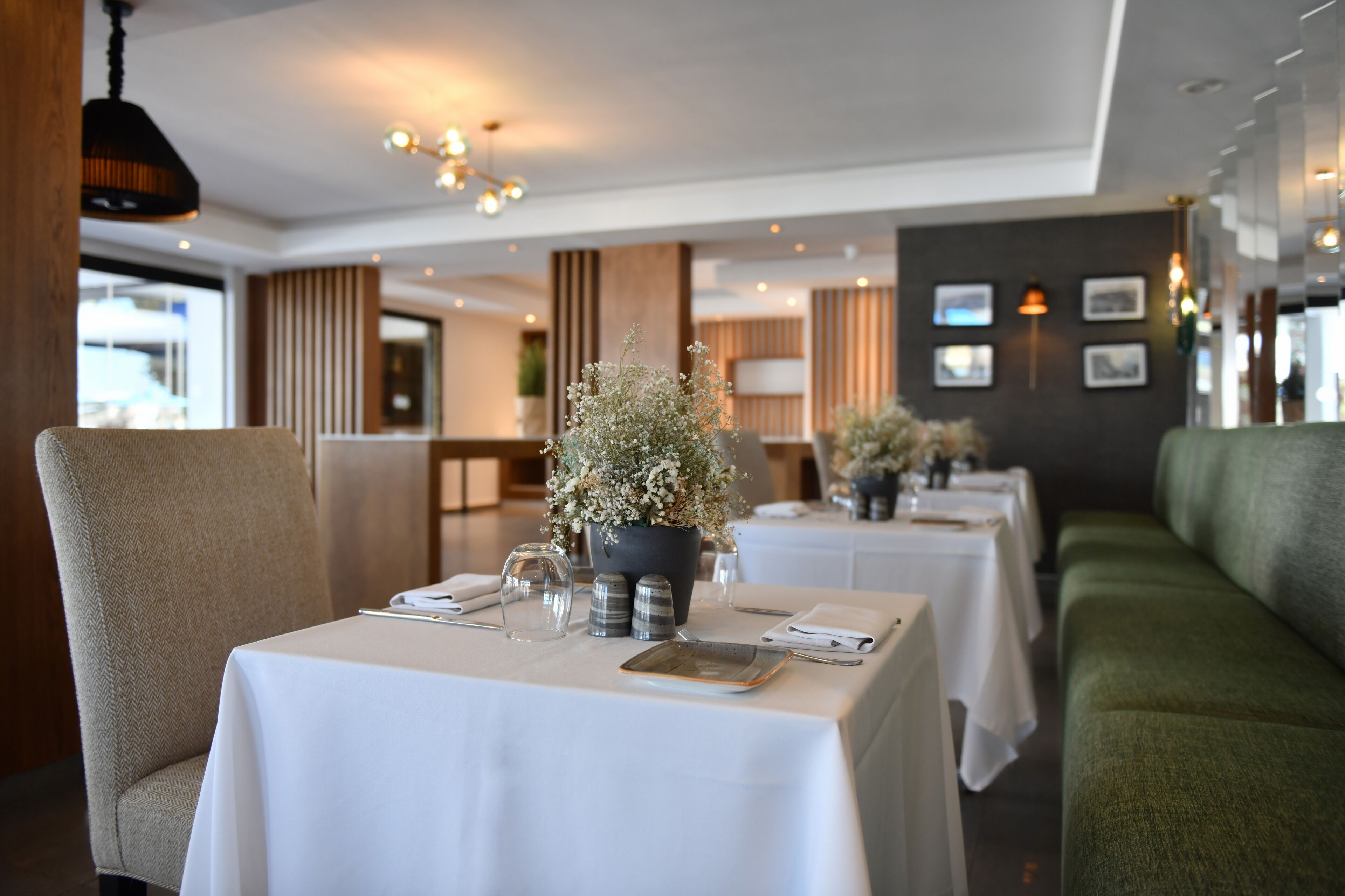 A restaurant with white tablecloths, neatly set tables, and a green sofa.