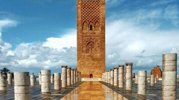 Una alta torre de ladrillo con fachada decorada, rodeada de columnas regularmente espaciadas sobre un camino empedrado.