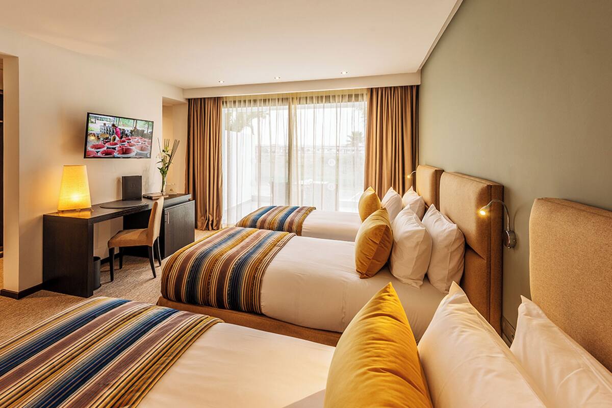 A hotel room with two beds, a desk, a TV, and a view of the outdoors.