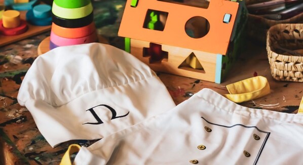 A white chef's jacket with a large letter 'R' on the front, a wooden toy house, and colorful containers on a table. - Dawliz Rabat Art & Spa (Salé)