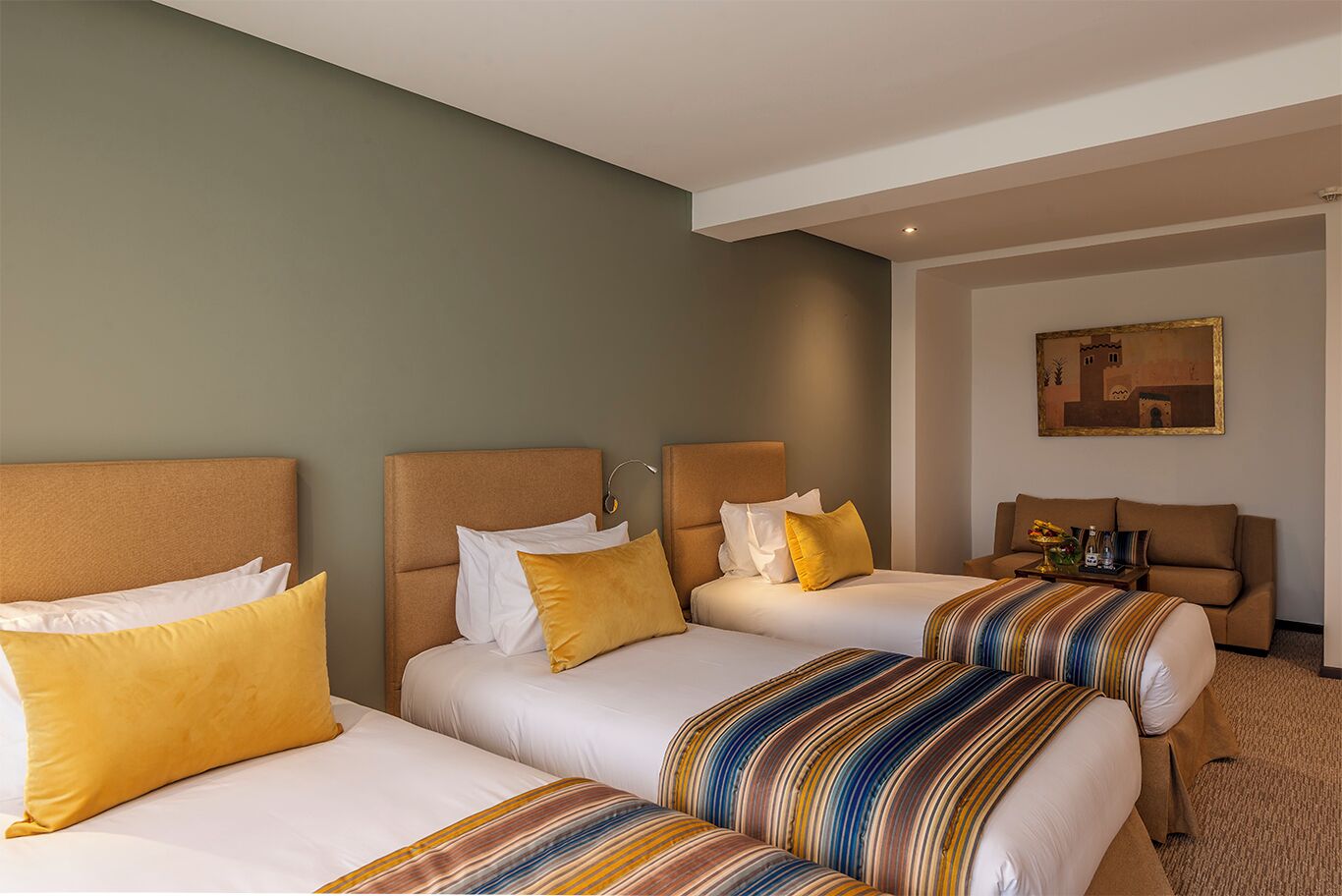 A hotel room with two beds, each with white linens and striped blankets, a beige sofa, and a painting on the wall.