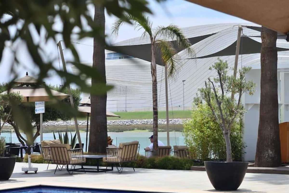 A pool area with lounge chairs, a palm tree, and a view of the beach.