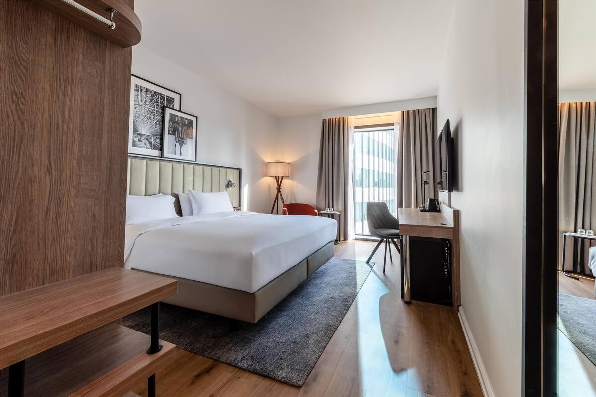 A modern hotel room with a large bed, a desk, a chair, and a television.