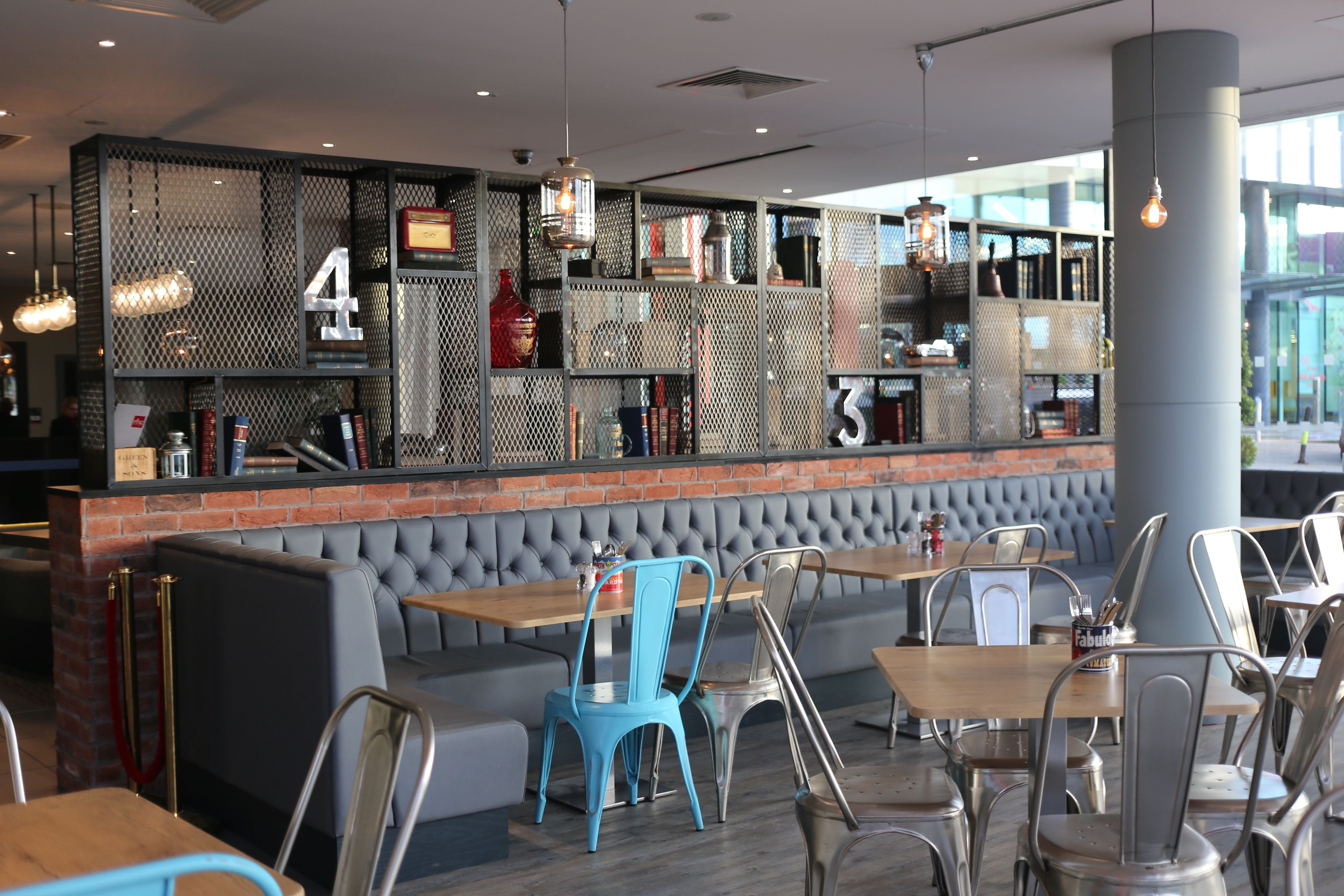 A restaurant with a brick wall, cushioned seating, and metal chairs.