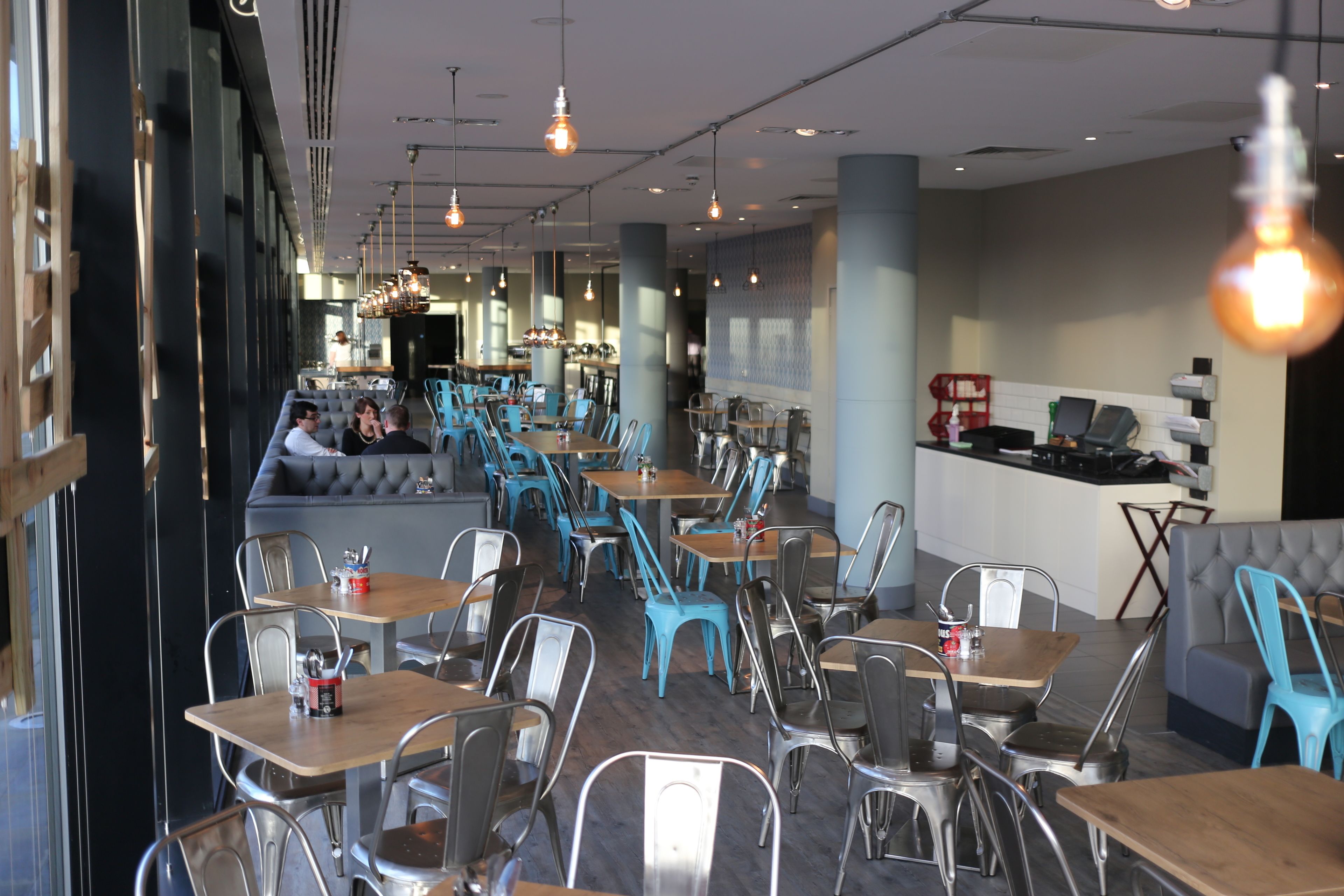 A restaurant with multiple tables and chairs, a bar area, and a seating section with a cushioned bench.