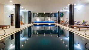 En moderne swimmingpool indendørs med et centralt siddeområde, liggestole og klart vand.