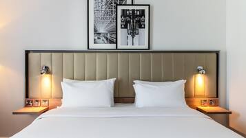 Una cama bien hecha con sábanas blancas, dos mesitas de noche con lámparas, y dos fotografías en blanco y negro enmarcadas en la pared sobre la cama.