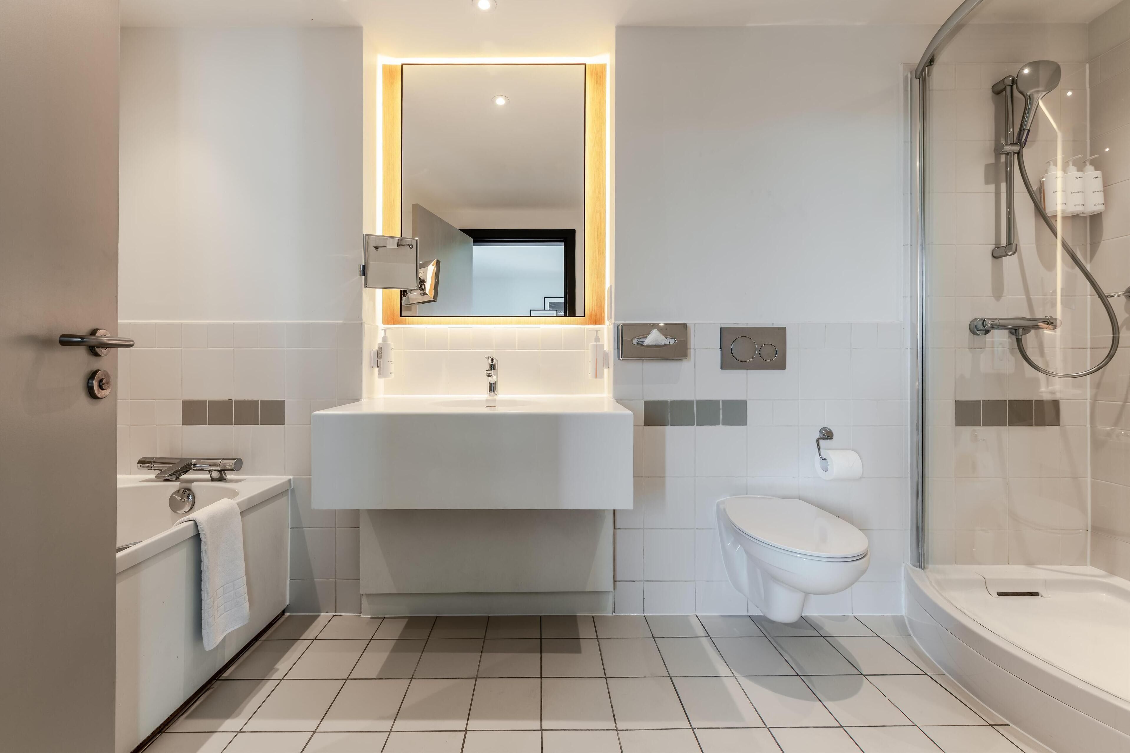 A modern bathroom with a white sink, a mirror, a shower, and a toilet.
