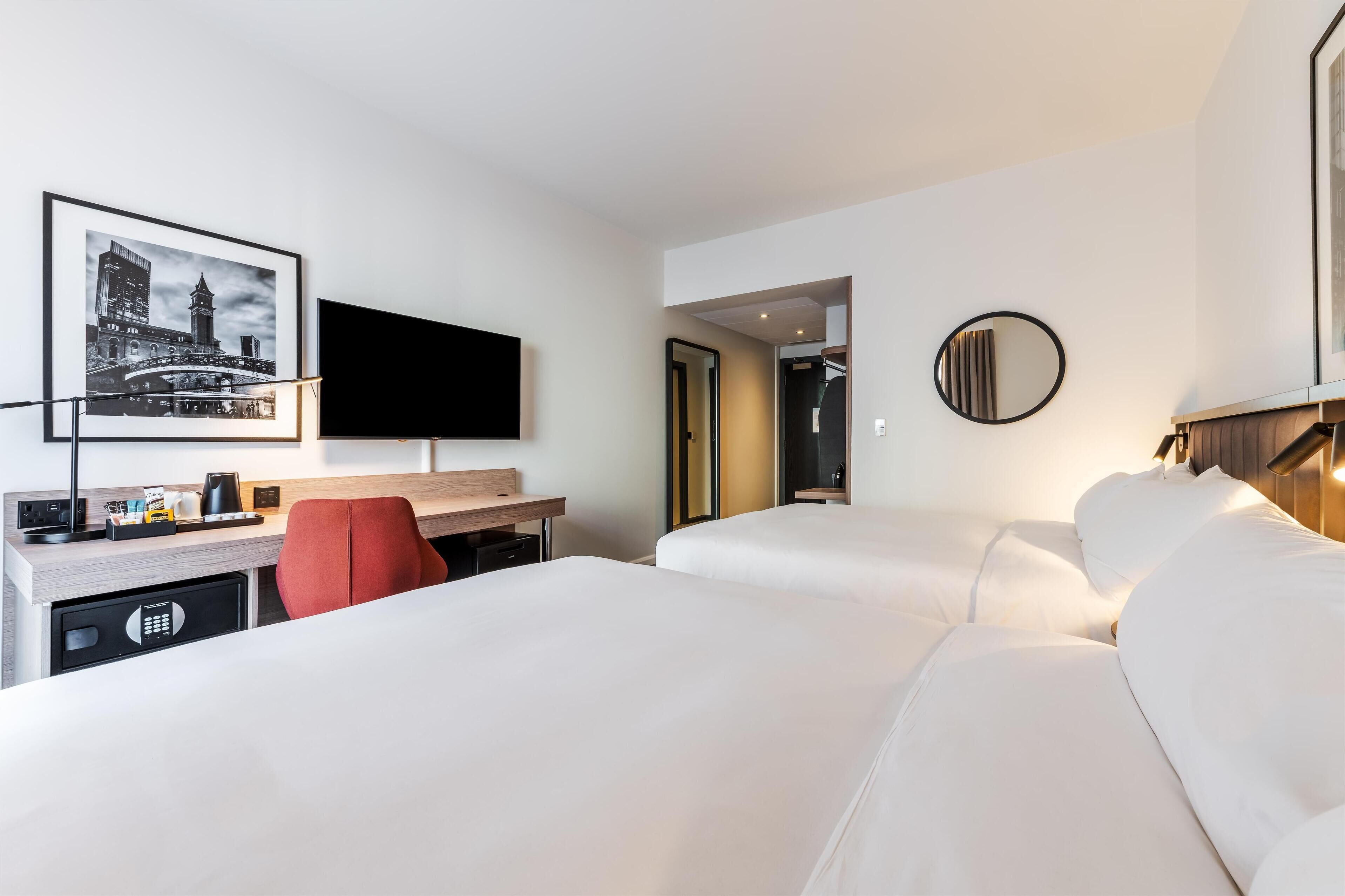 A hotel room with two beds, a desk with a chair, a TV, and a framed picture on the wall.