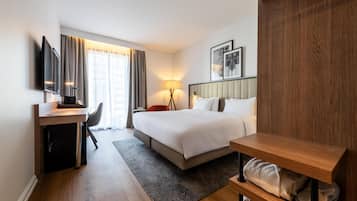 A hotel room with a bed, a desk, a chair, a lamp, and a TV.