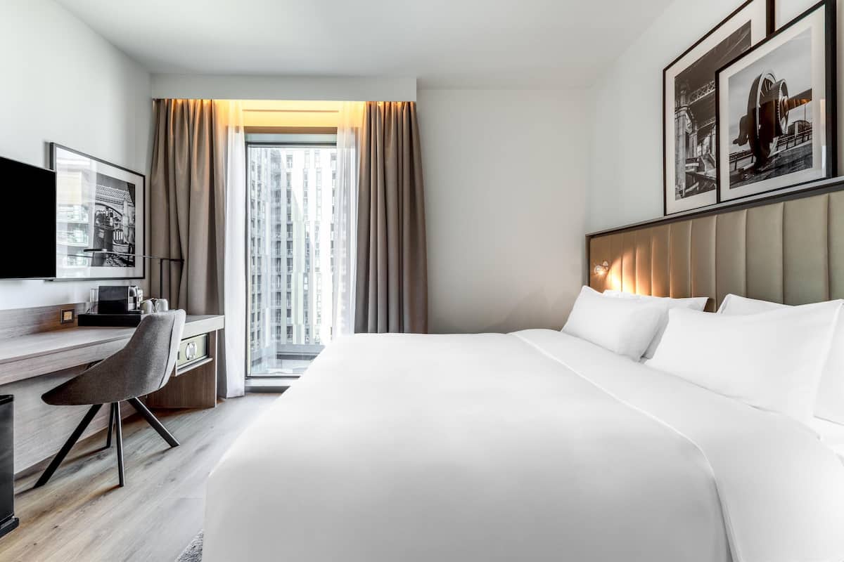 A modern hotel room with a large bed, a desk with a chair, a television, and framed pictures on the wall.