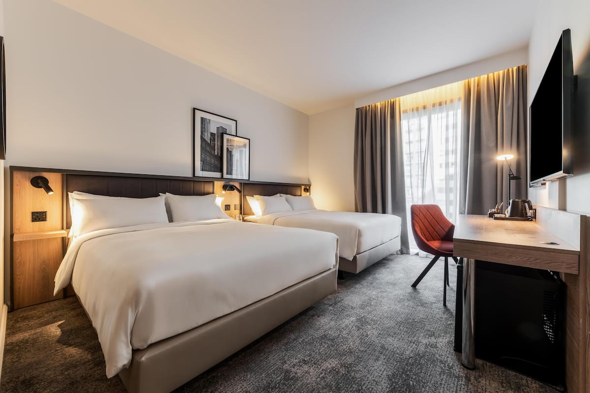 A hotel room with two beds, a desk, a chair, a TV, and a picture on the wall.