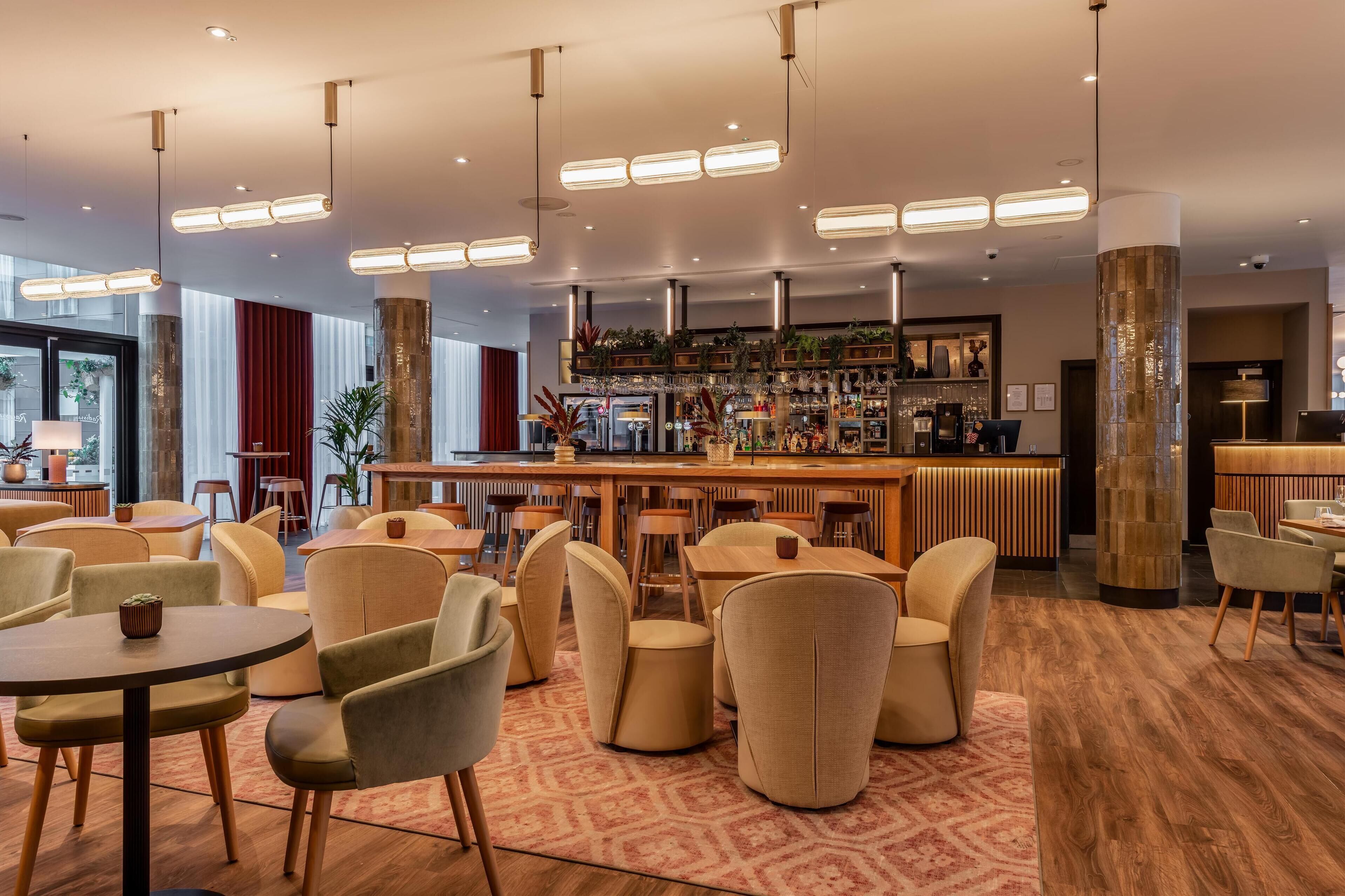 Un espace bar moderne offrant de nombreuses options de sièges, notamment des tables rondes et des chaises rembourrées, ainsi qu'un comptoir de bar proposant une variété de boissons et d'en-cas.