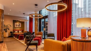 En moderne lobby med siddeområde, receptionsdisk og store vinduer med røde gardiner.