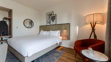 A modern hotel room with a large bed, a red armchair, a small table, and a floor lamp.