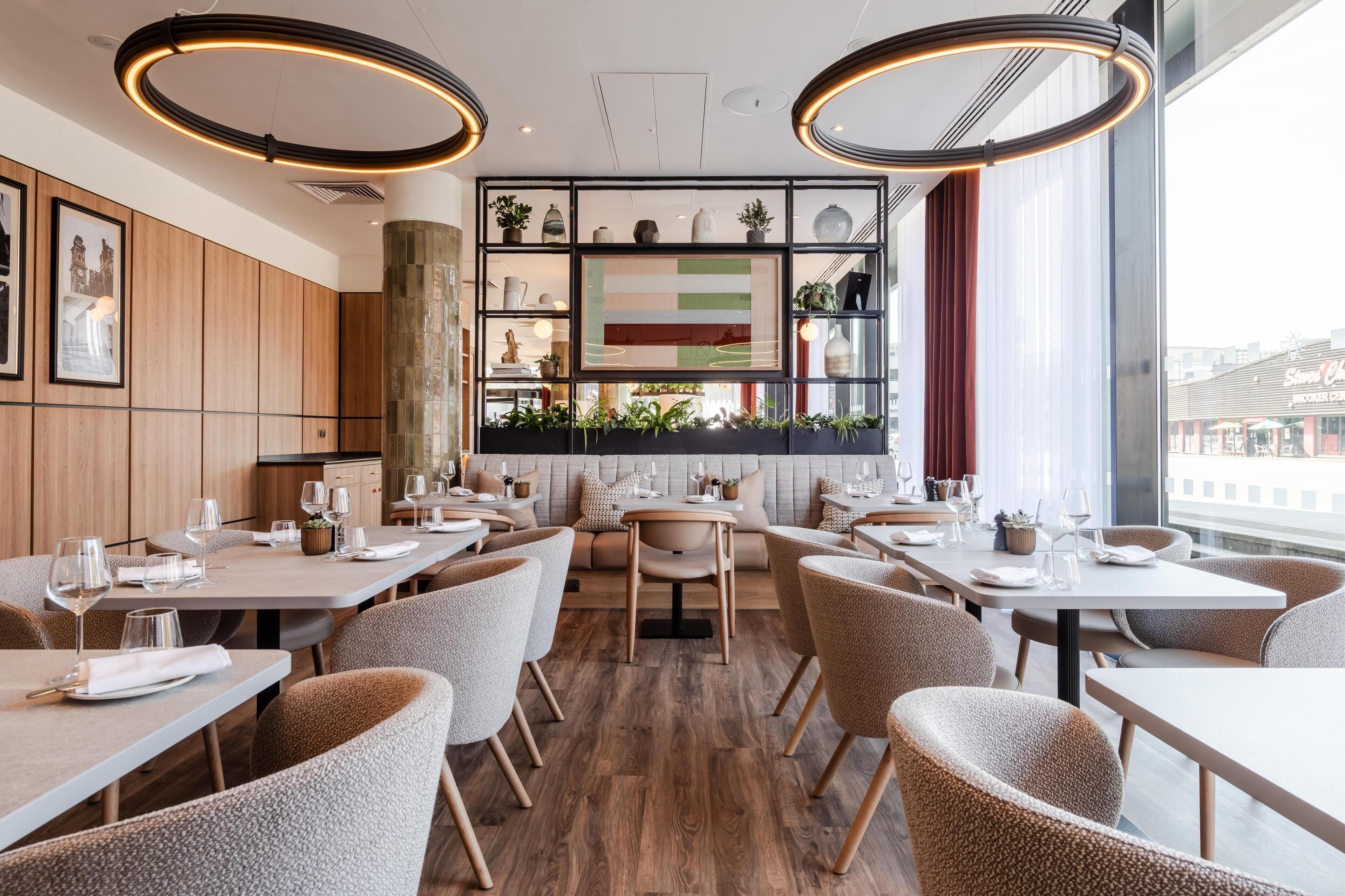 A modern restaurant interior with wooden panel walls, round tables, and chairs.