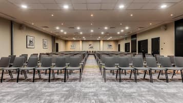 Un salón de conferencias con filas de sillas, piso alfombrado y cuadros en las paredes.