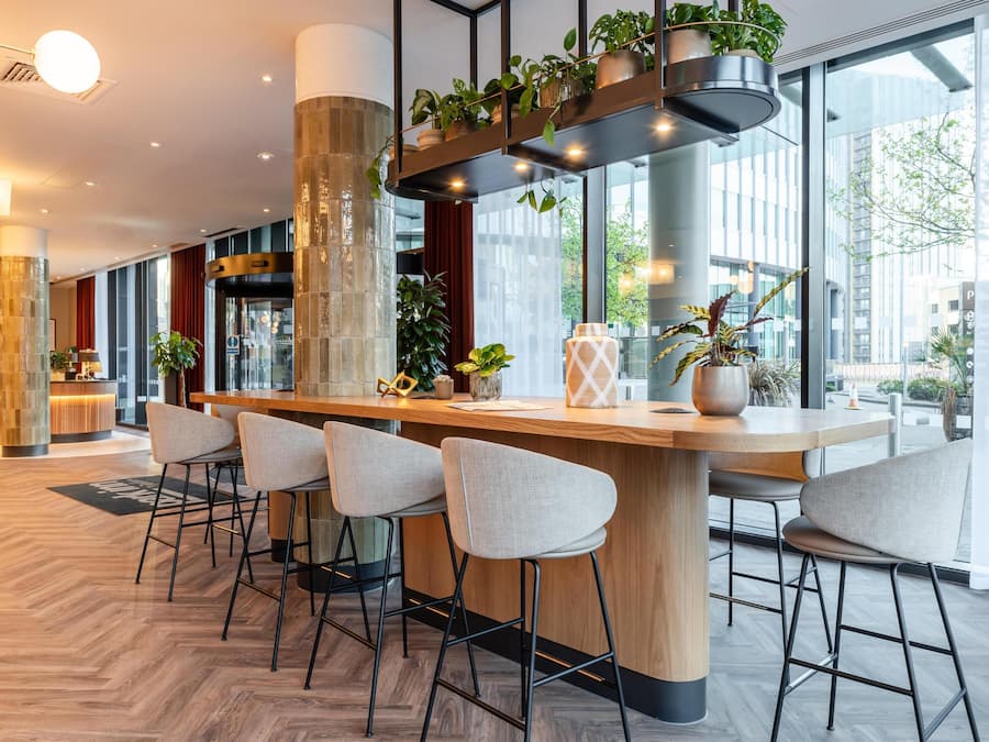 A modern bar area with a wooden counter, bar stools, and potted plants.