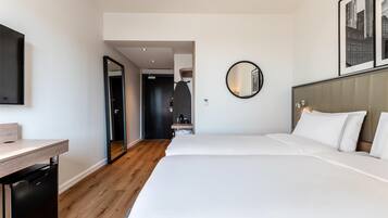 A hotel room with a bed, a desk, a mirror, and a door leading to another room.