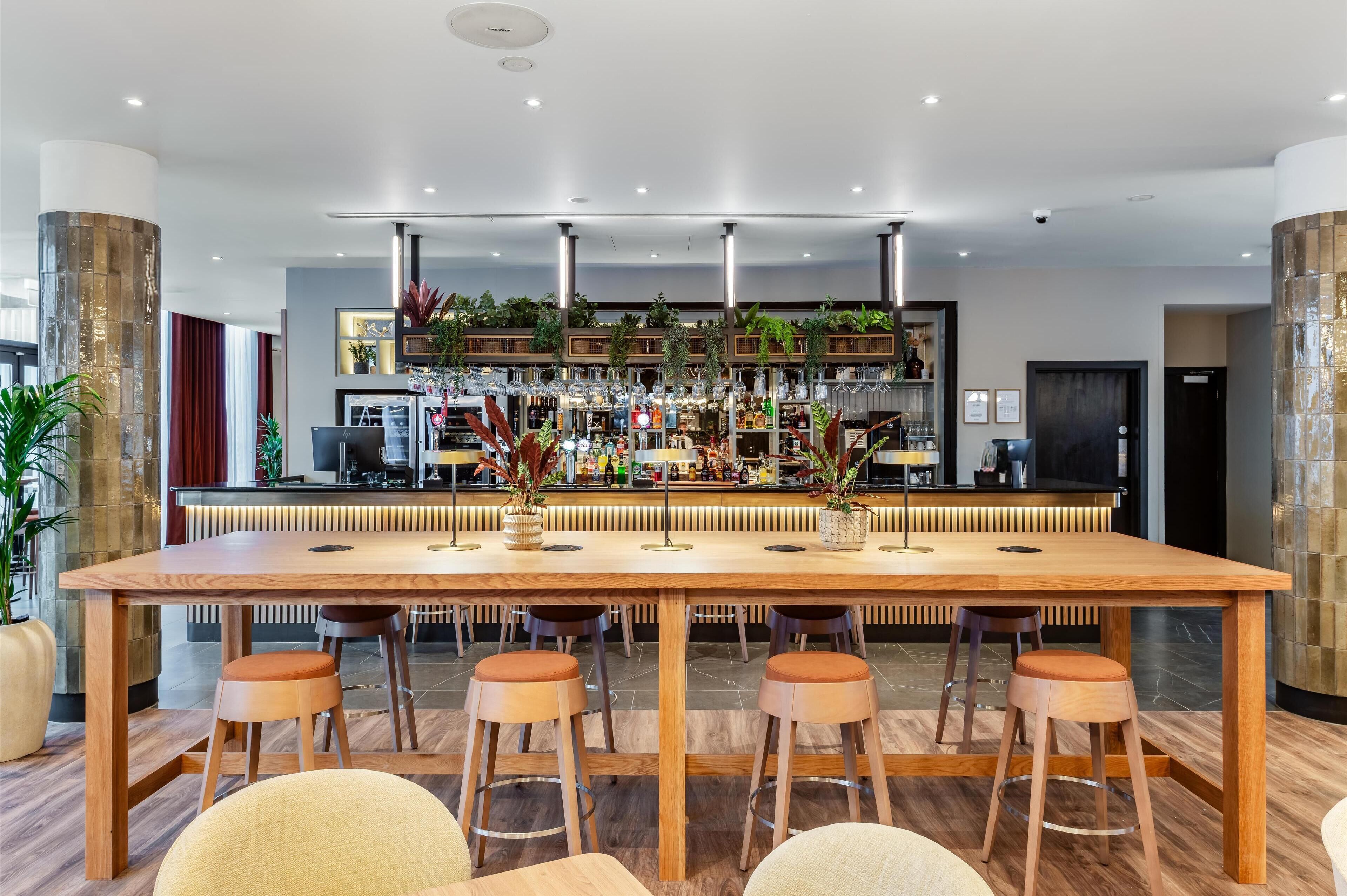 Eine moderne Bar mit einem langen Holztisch, Barhocker und einer gut sortierten Bar.