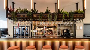 Et barområde med trælampebænk, en bar med glas og hylder med planter og flasker.